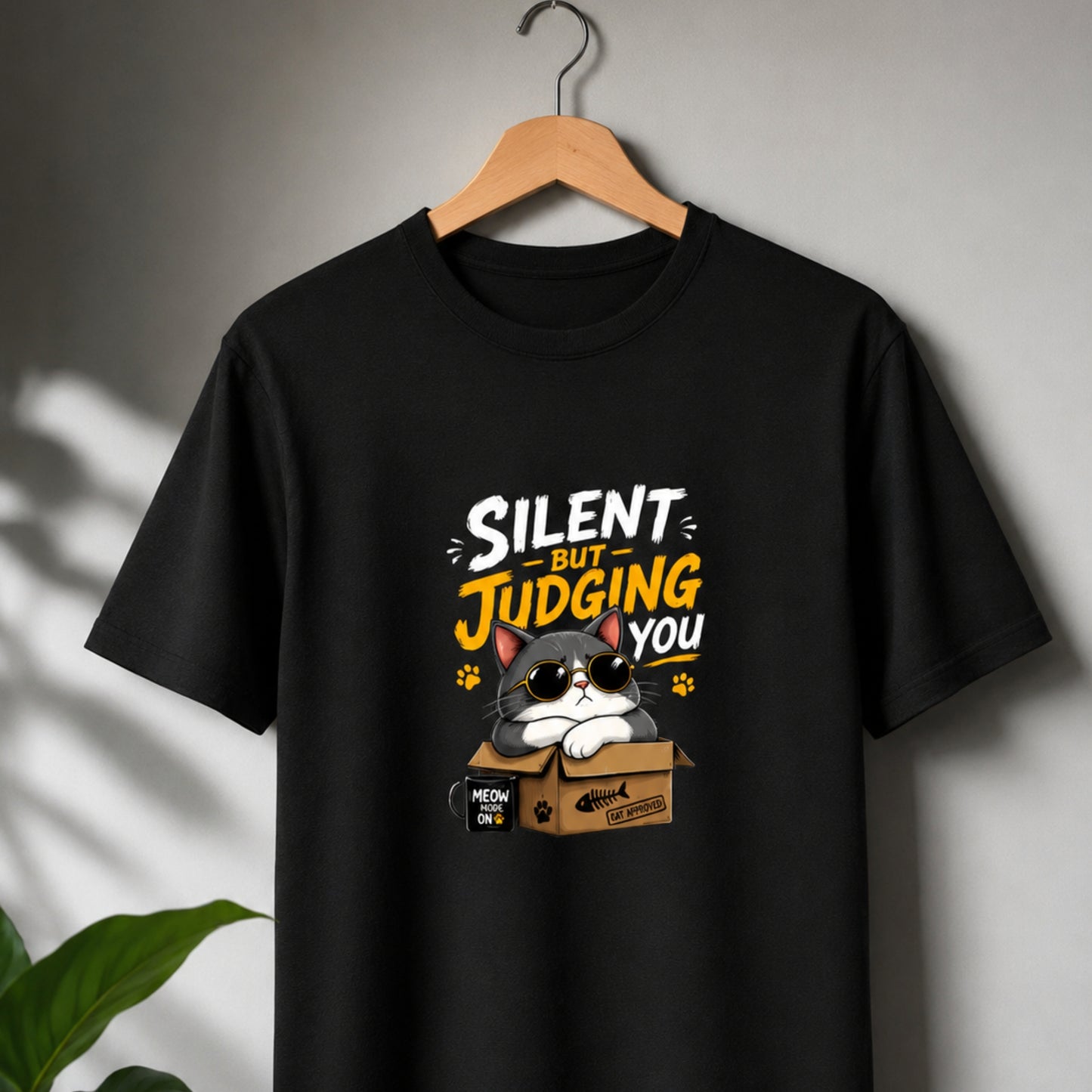 Black t-shirt with a cat graphic and text 'Silent but judging you' on a hanger against a gray background.