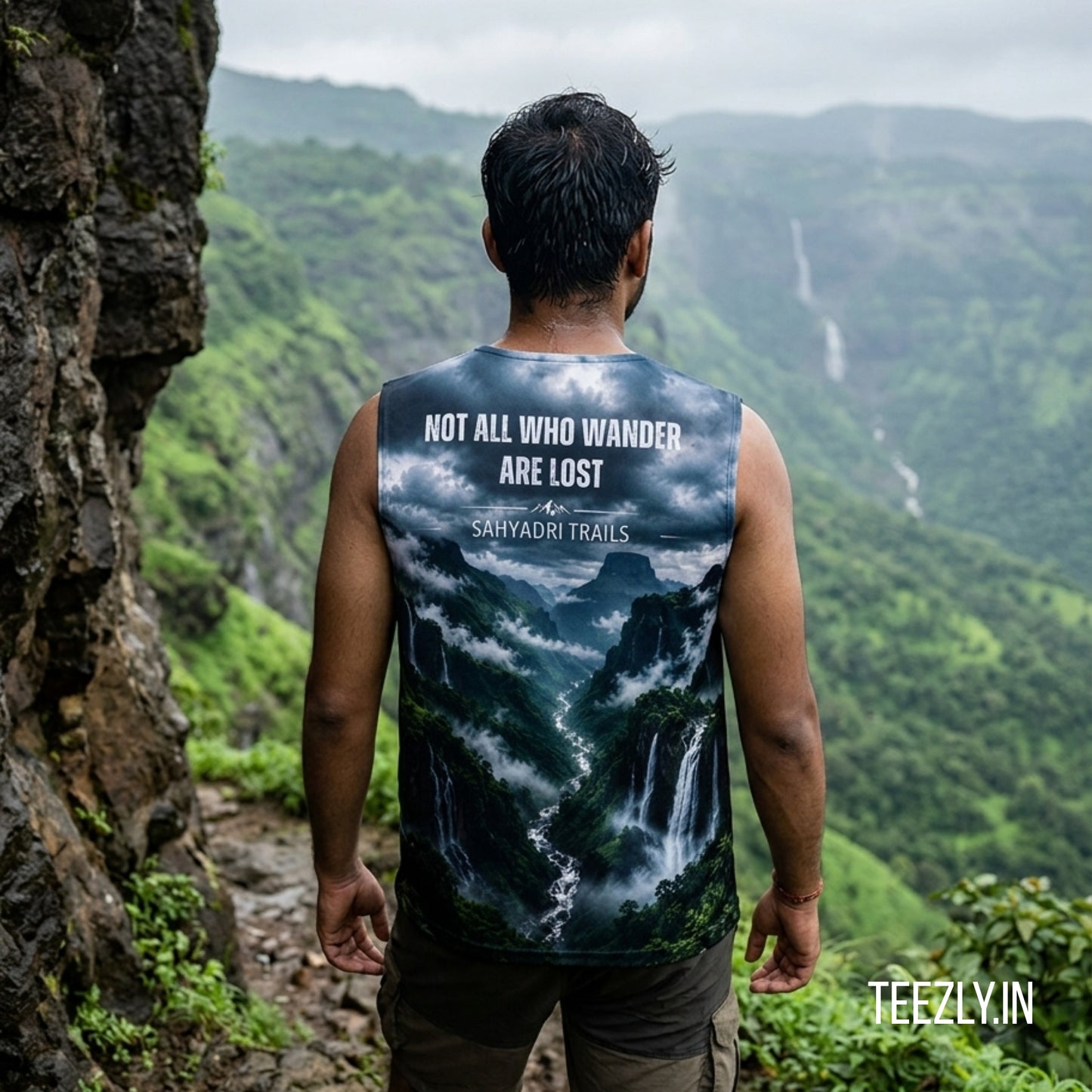 Person wearing a sleeveless shirt with a mountain design and text, standing in a scenic location.