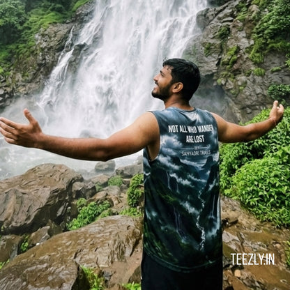 Man with arms outstretched in front of a waterfall, wearing a tank top with text.