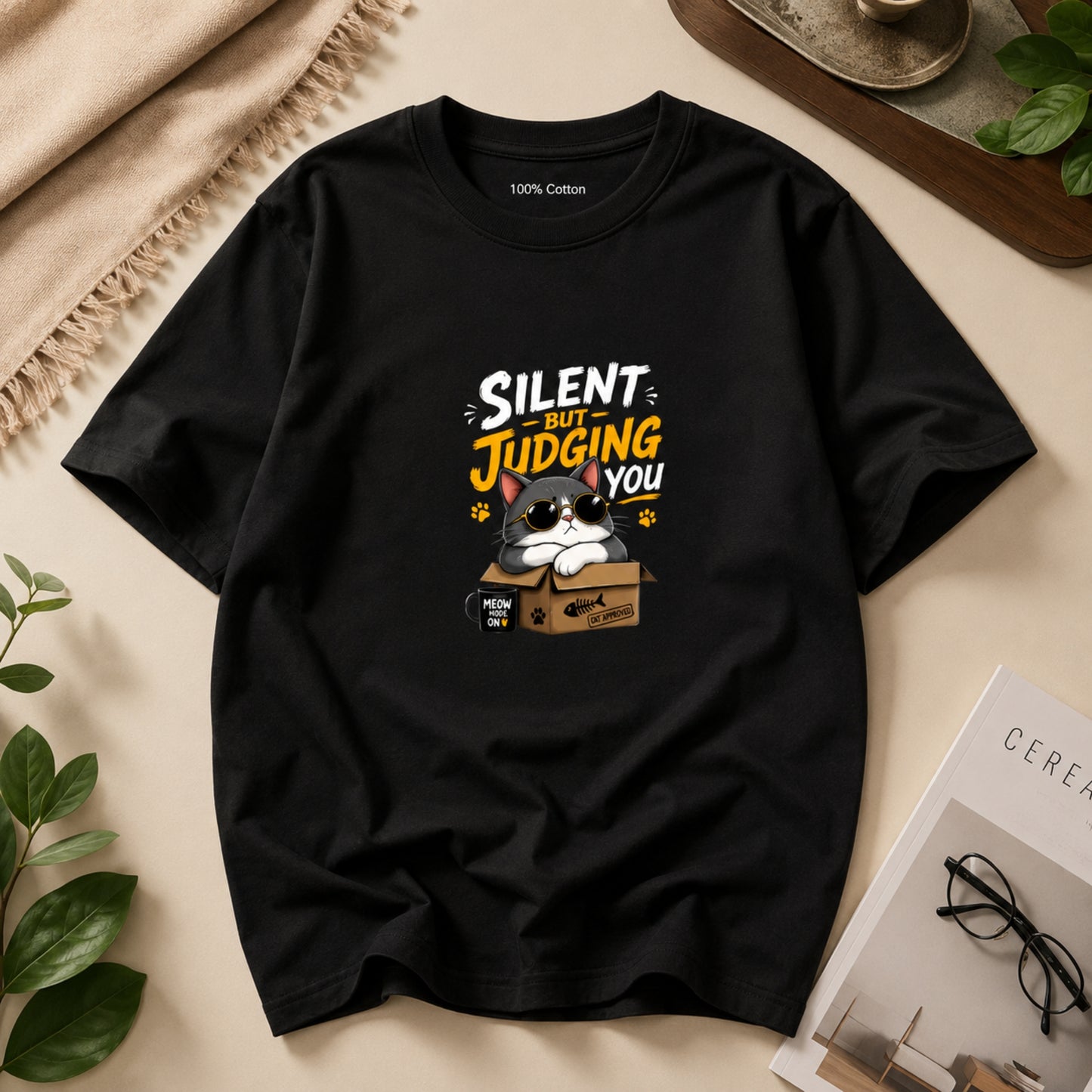 Black t-shirt with a cat graphic and text 'Silent but judging you' on a beige surface.