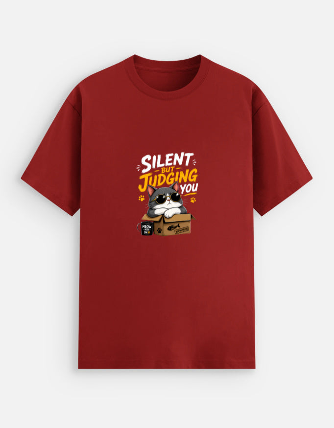 Red unisex stretch t-shirt featuring a cute sunglasses-wearing cat sitting on a box with the text “Silent But Judging You” in bold yellow and white typography, humorous meme-style graphic design on chest.