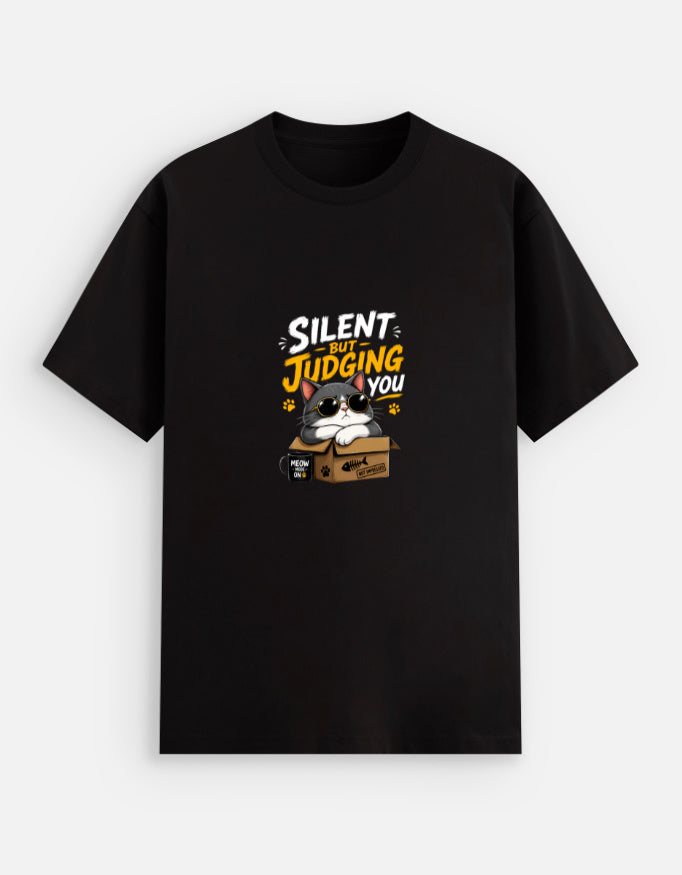 Black unisex stretch t-shirt featuring a cute sunglasses-wearing cat sitting on a box with the text “Silent But Judging You” in bold yellow and white typography, humorous meme-style graphic design on chest.