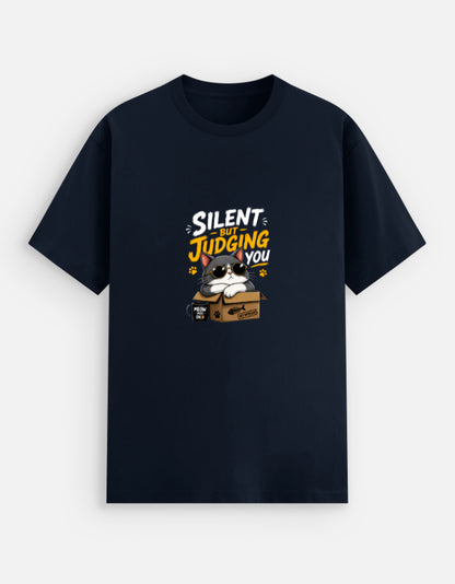 Navy Blue unisex stretch t-shirt featuring a cute sunglasses-wearing cat sitting on a box with the text “Silent But Judging You” in bold yellow and white typography, humorous meme-style graphic design on chest.