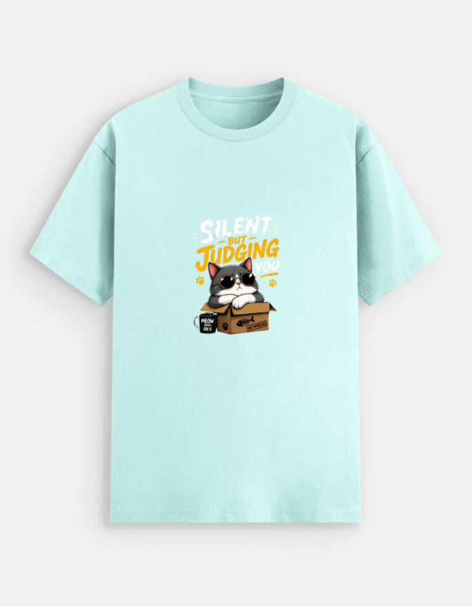 Mint unisex stretch t-shirt featuring a cute sunglasses-wearing cat sitting on a box with the text “Silent But Judging You” in bold yellow and white typography, humorous meme-style graphic design on chest.